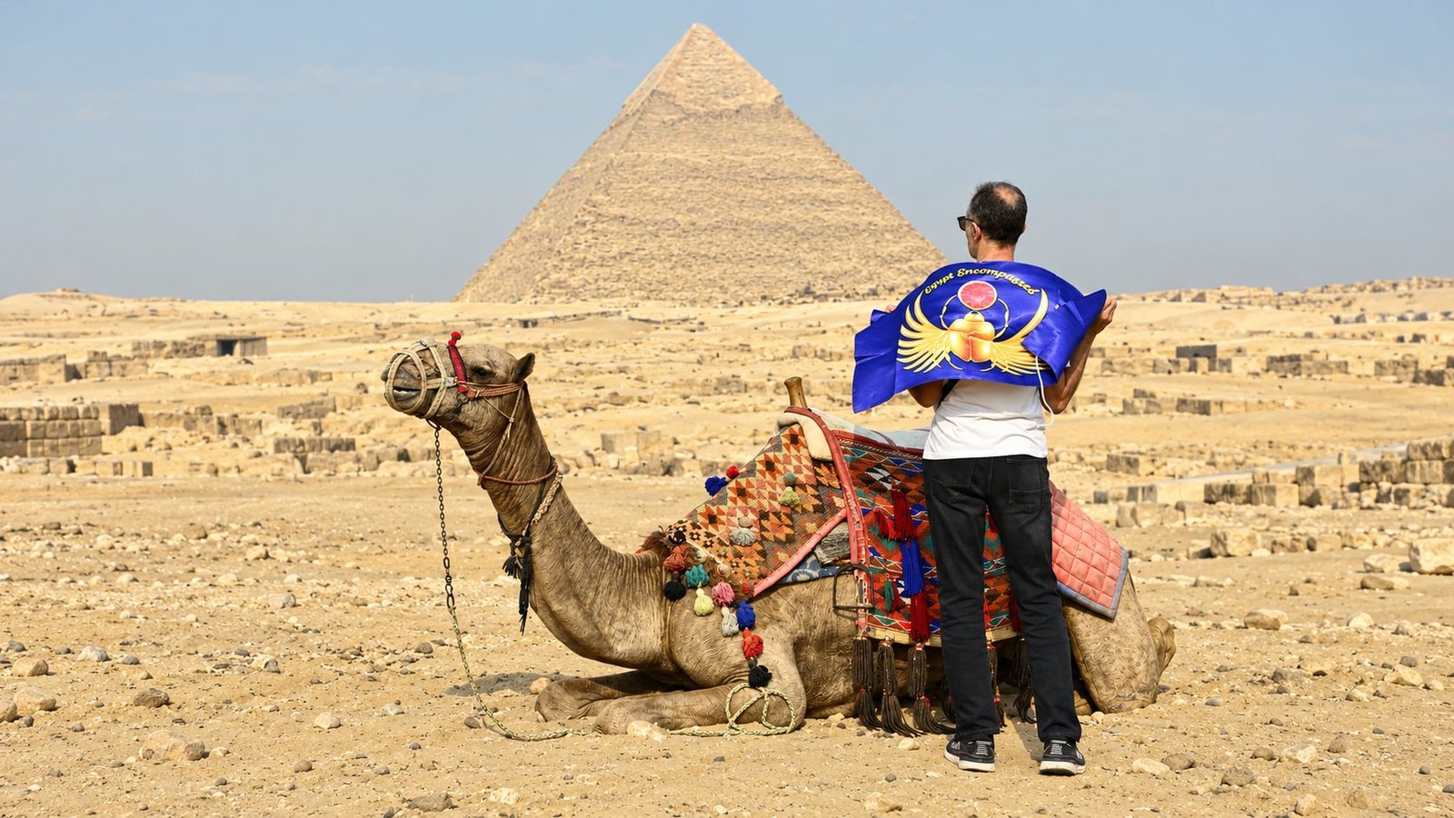 Guest holding an Egypt Encompassed flag beside a camel and the Pyramid of Khafre